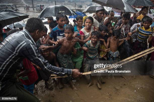 Man hits anxious Rohingya children with a cane as things get out of control during a humanitarian aid distribution while monsoon rains continue to...