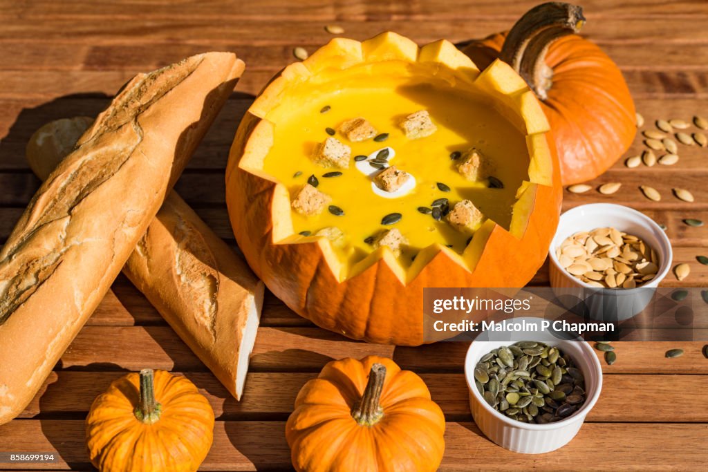Pumpkin soup in shell served with bread and roasted pumpkin seeds