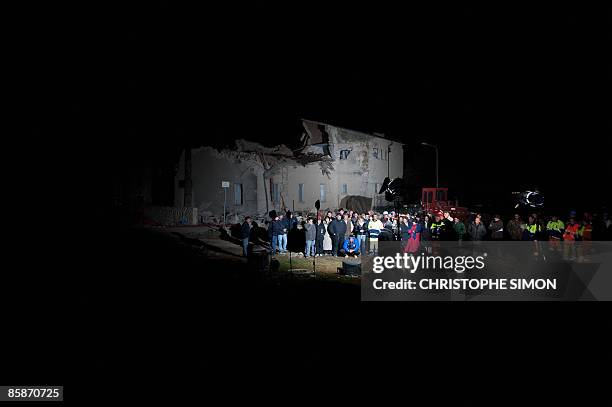 Quake survivors watch a news programme on a television set placed on the ground, as a journalist waits for a live broadcast at the entrance of Onna,...