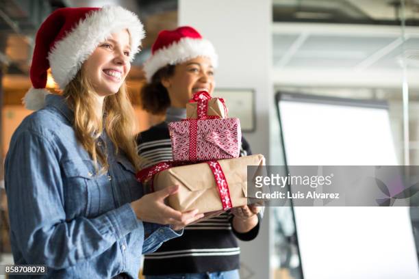 smiling businesswomen holding christmas gifts in office - christmas party office stock-fotos und bilder