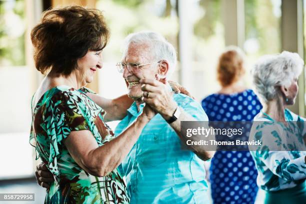 smiling seniors dancing together in community center - active seniors dancing stock pictures, royalty-free photos & images