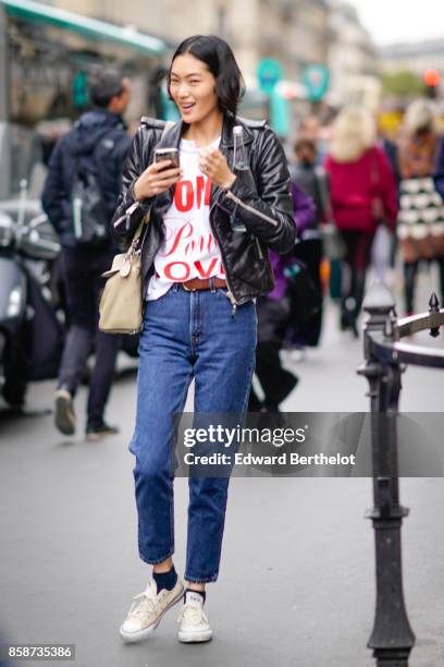 Model wears a black leather jacket, blue pants, white sneakers, outside Stella Mccartney, during Paris Fashion Week Womenswear Spring/Summer 2018, on...