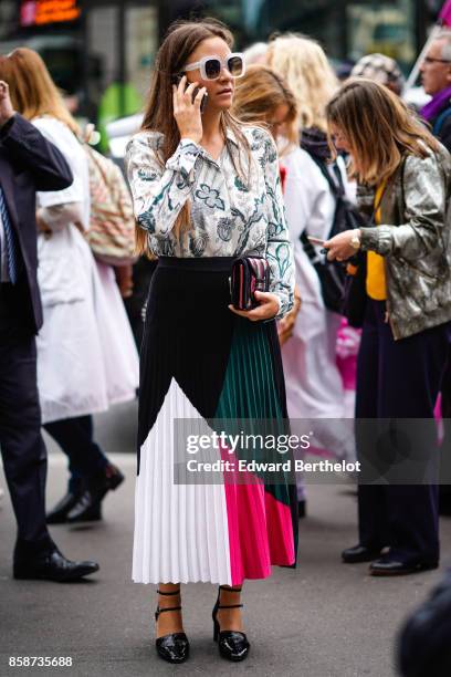Guest wears a flower print shirt, a pleated color skirt, uses a smartphone, outside Stella Mccartney, during Paris Fashion Week Womenswear...