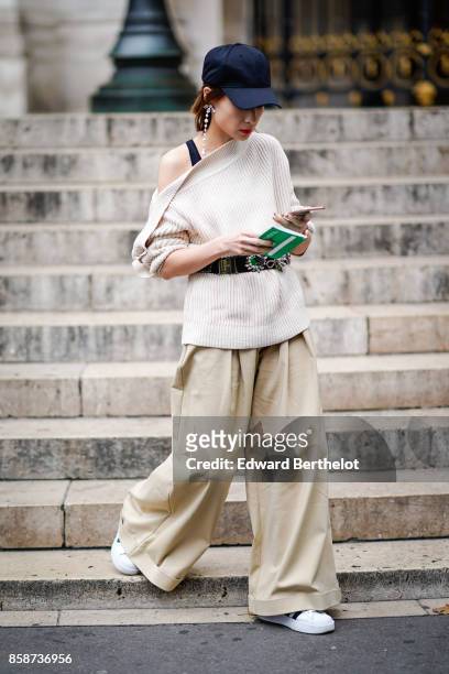 Guest wears a cap, an off shoulder top, a belt, beige pants, white sneakers , outside Stella Mccartney, during Paris Fashion Week Womenswear...