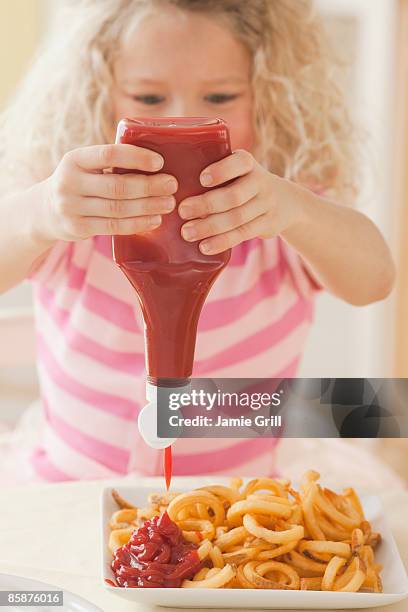 young girl squeezing ketchup on french fries - ketchup stock-fotos und bilder