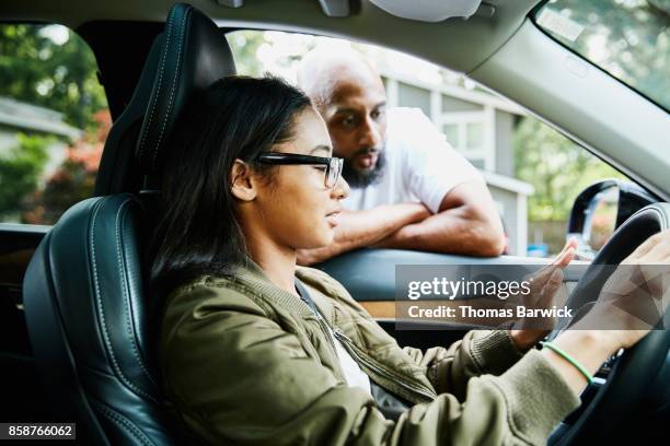 father leaning through window of car while teaching daughter to drive - girl driving imagens e fotografias de stock