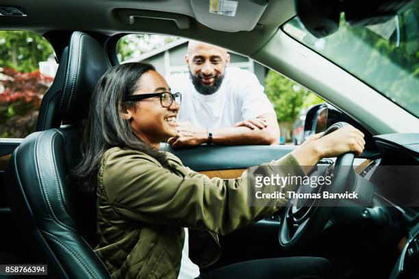 smiling father leaning in car window giving instructions for daughter learning to drive - beautiful asian girls stock pictures, royalty-free photos & images
