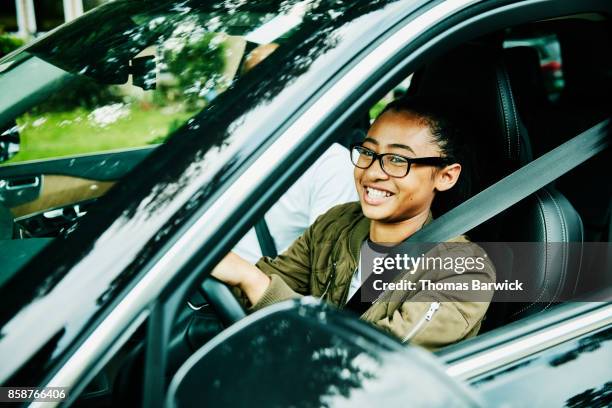 laughing young woman in drivers seat of car taking driving lesson from father - seat belt stock-fotos und bilder