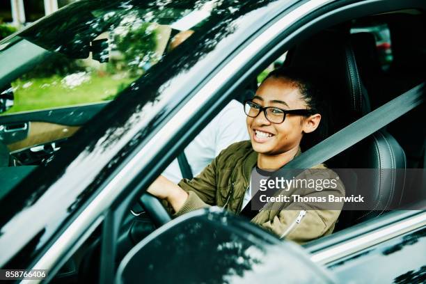 Laughing young woman in drivers seat of car taking driving lesson from father