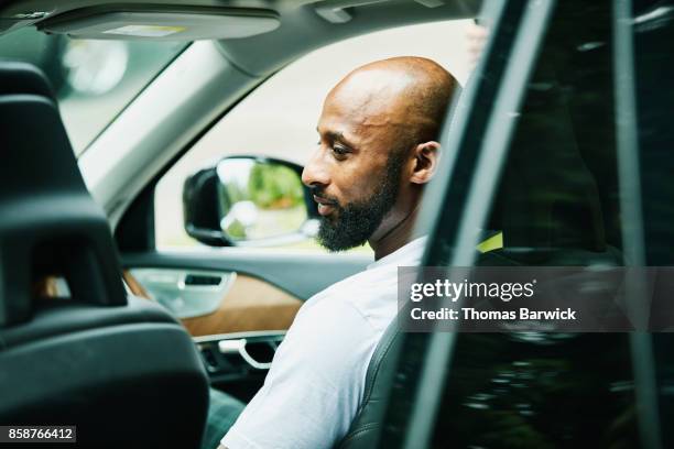 smiling man seated in passenger seat of car waiting - black car photos et images de collection