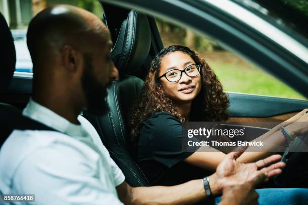 smiling young woman seated in drivers seat of car listening to fathers advice while taking driving lesson - daughter driving stock pictures, royalty-free photos & images