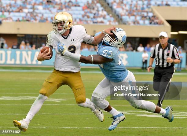 Ian Book of the Notre Dame Fighting Irish stiff-arms Malik Carney of the North Carolina Tar Heels during the game at Kenan Stadium on October 7, 2017...