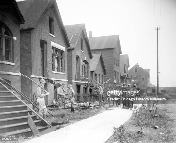 Soldiers stand guard with rifles at a house vandalized during the race riots of July-August 2, 1919 in Chicago, Illinois. A group of white adults and...