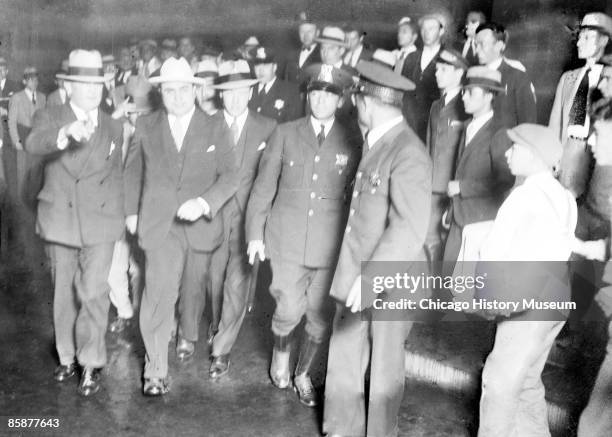 View of Al Capone striding along escorted by police and unidentified men around the time of his trial, Chicago, 1931.