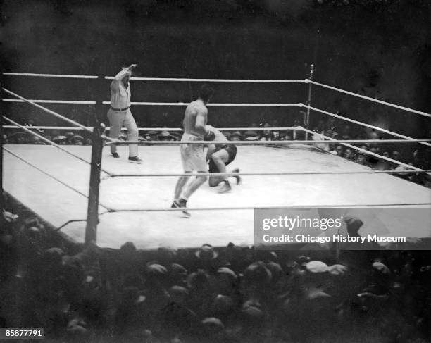 Boxer Jack Dempsey kneels on the mat in a boxing ring during a bout against Gene Tunney at Soldier Field, Chicago, 1927. Tunney is standing in the...