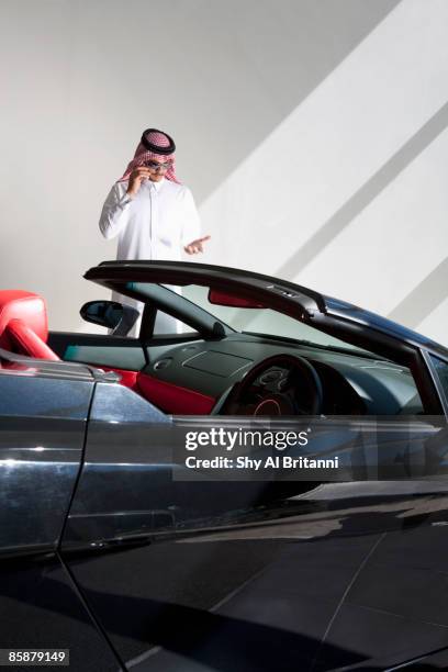 arab man standing besides car talking on his mobile phone. - arab car stock pictures, royalty-free photos & images