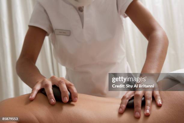 female masseur placing therapeutic hot stones on woman's back. - emirati lady from back stock-fotos und bilder