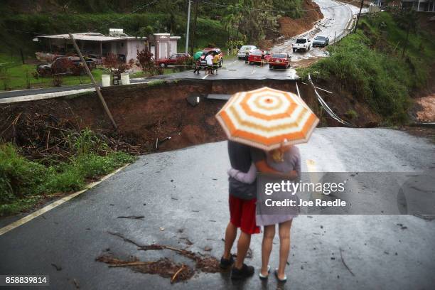People look on at a section of a road that collapsed and continues to erode days after Hurricane Maria swept through the island on October 7, 2017 in...