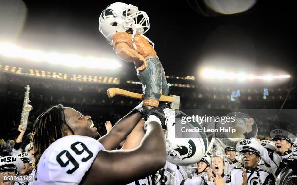 Raequan Williams of the Michigan State Spartans celebrates a win over the Michigan Wolverines and carries the Paul Bunyan trophy after the game at...