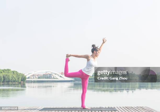 young woman exercising yoga on lake pier - lord of the dance pose stock pictures, royalty-free photos & images