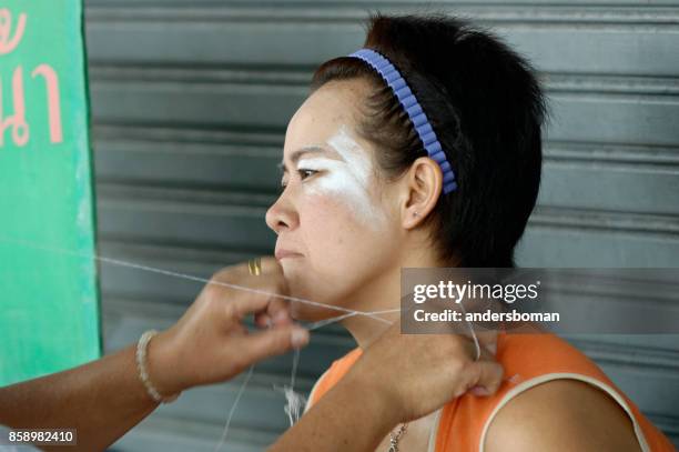 woman in bangkok gets facial hair removal runt eyebrows threading procedure - threading stock pictures, royalty-free photos & images