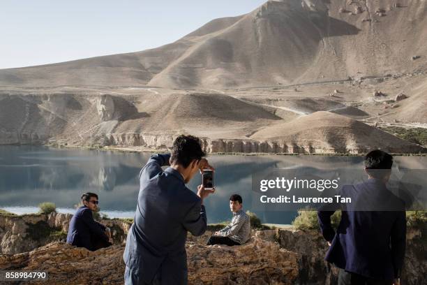 Group of Afghan teachers from Kabul take photos with the Band-e Haibat lake seen in the background during their visit to Band-e Amir national park on...