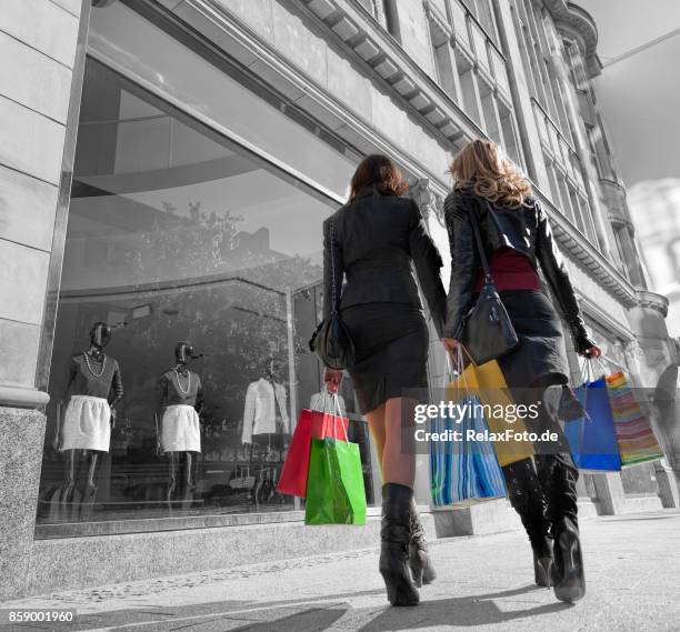 achteraanzicht op twee jonge vrouwen met boodschappentassen wandelen in voetgangersgebied langs winkel venster - geïsoleerde kleur stockfoto's en -beelden