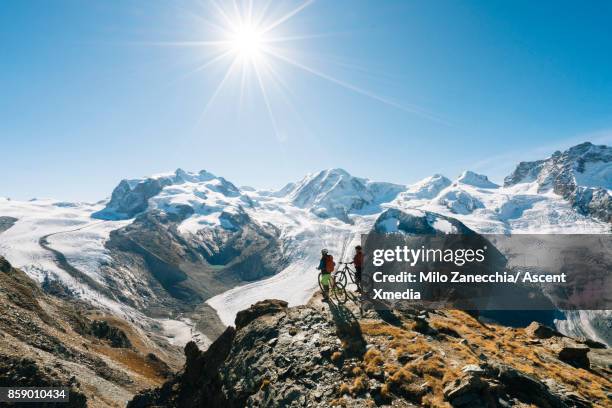 female mountain bikers look off to snow capped mountain range, from edge - euforie stockfoto's en -beelden