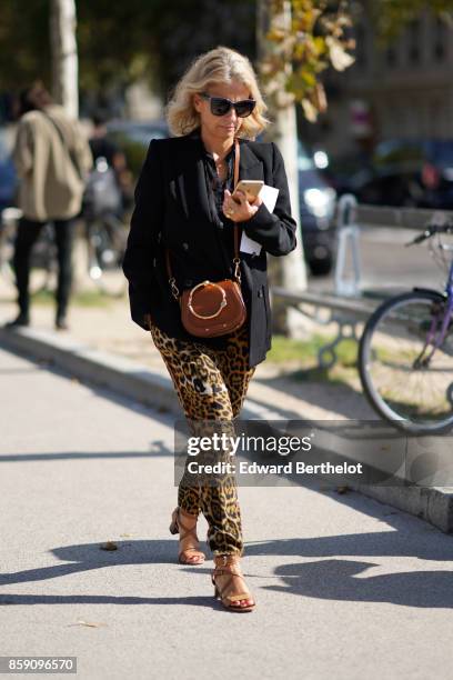 Guest wears a black blazer jacket, a bag, leopard print pants and brown shoes, outside Nina Ricci, during Paris Fashion Week Womenswear Spring/Summer...