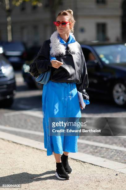 Guest wears a blue pleated skirt, a black leather jacket with white fur, red sunglasses, black shoes, outside Nina Ricci, during Paris Fashion Week...