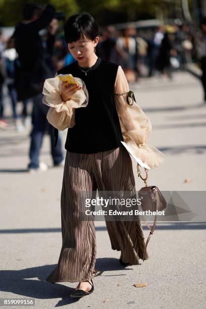 Guest wears a top with ruffle lace sleeves, pleated pants, outside Nina Ricci, during Paris Fashion Week Womenswear Spring/Summer 2018, on September...