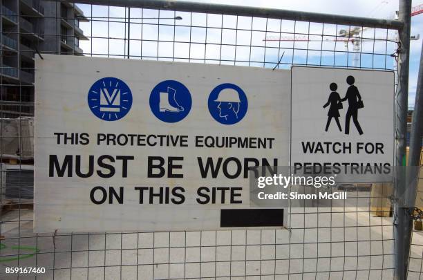 signs reminding construction workers to wear protective equipment, and watch out for pedestrians, on a construction site for a residential apartment building - stiefel-mit-stahlkappen stock-fotos und bilder