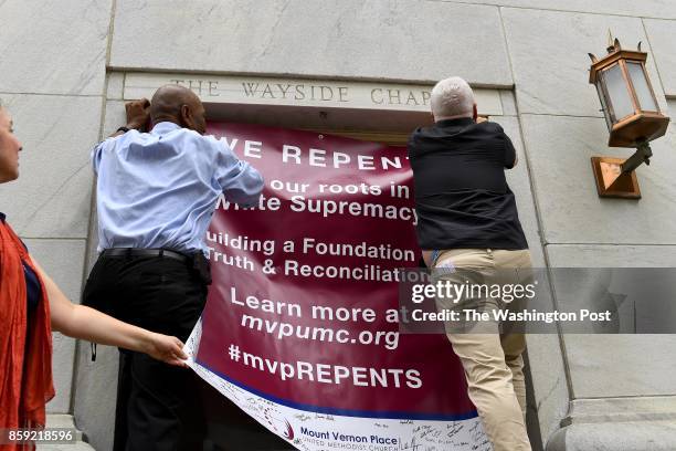 Richardson and Thomas Mills hang a banner while Kimberly Burge lends a hand at the cornerstone of Mount Vernon Place United Methodis Church, signed...