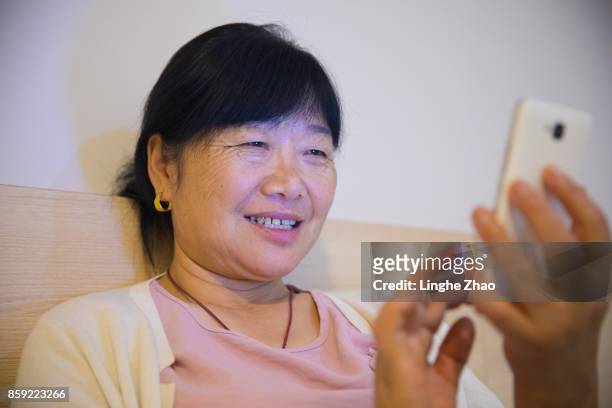 senior woman using mobile phone on bed - linghe zhao stock pictures, royalty-free photos & images