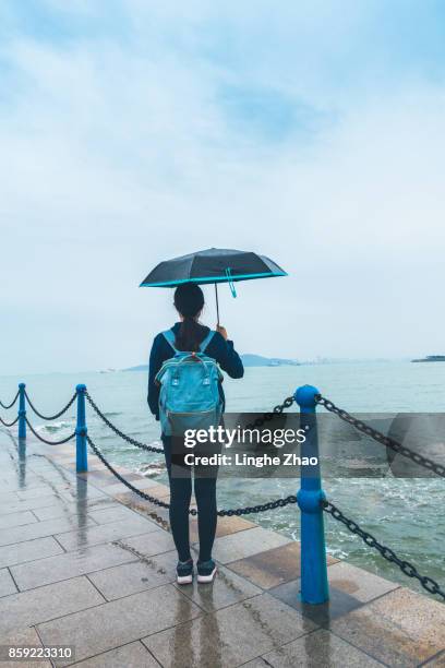 young woman holding up an umbrella by sea - linghe zhao photos et images de collection