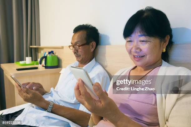 asian senior couple using mobile phone on bed - linghe zhao photos et images de collection