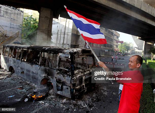 An anti-government protester waves a Thai flag next to a burnt out bus as members of the Thai military took over the streets during violent protests...
