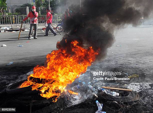 Anti-government protesters walk past a pile of buring tyres as gun battles break out during violent protests on April 13, 2009 in Bangkok, Thailand....