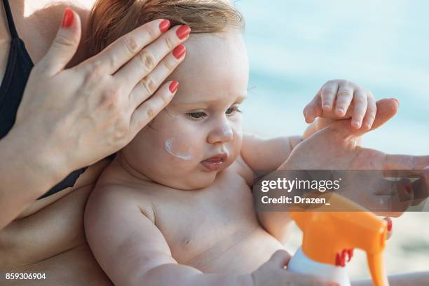 mother applying suntan lotion on her baby on the beach - baby suncream stock pictures, royalty-free photos & images