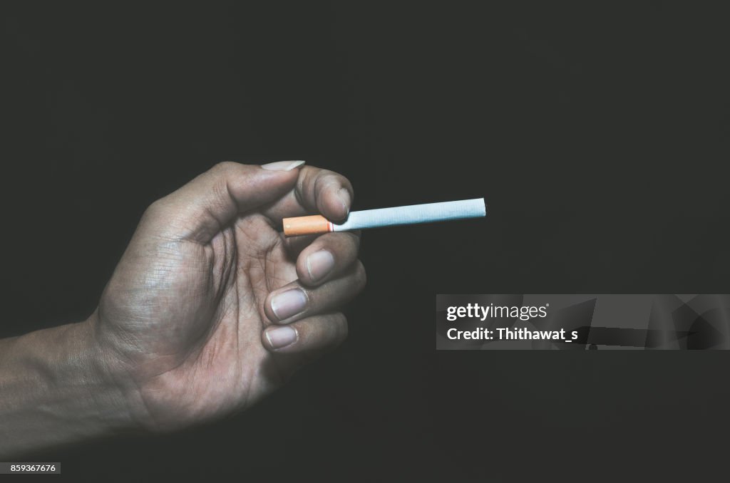 Cigarette in unhealthy hand man on black background low key.