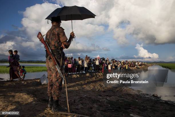 Bangladesh oder guards stand by as thousands of Rohingya refugees fleeing from Myanmar walk along a muddy rice field after crossing the border in...