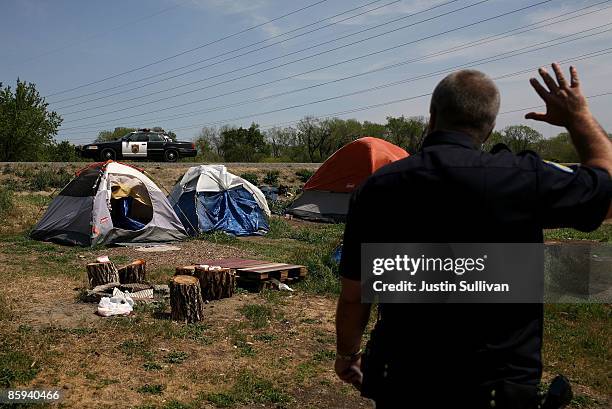 Sacramento police officer Mark Zoulas waves to a passing patrol car as he delivers eviction notices to residents at a homeless tent city April 13,...
