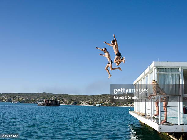 girl watching two men jumping off houseboat - house boat stock pictures, royalty-free photos & images