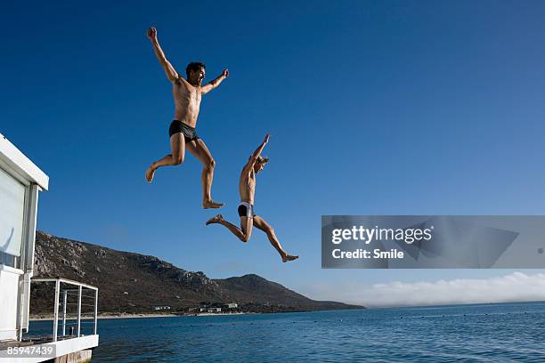 two men jumping off of houseboat - friends smile stock-fotos und bilder