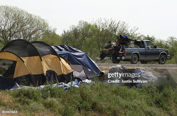 Homeless men ride on the back of a pickup truck carrying their belongings at a homeless tent city April 13, 2009 in Sacramento, California. Hundreds...