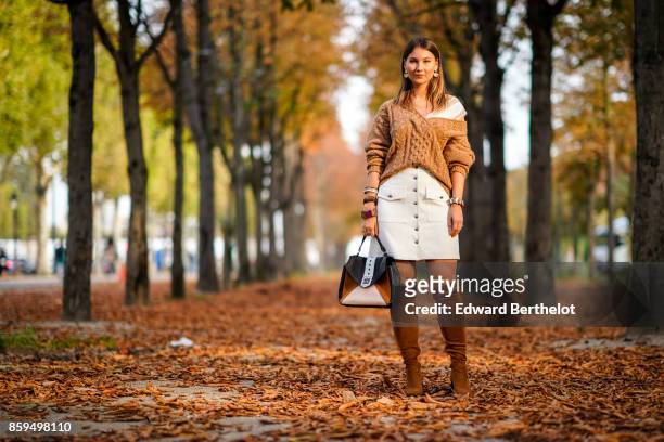 Angelica Ardasheva wears a camel V-neck pullover, a white skirt, camel boots and a black and camel bag, outside the Rochas show, during Paris Fashion...