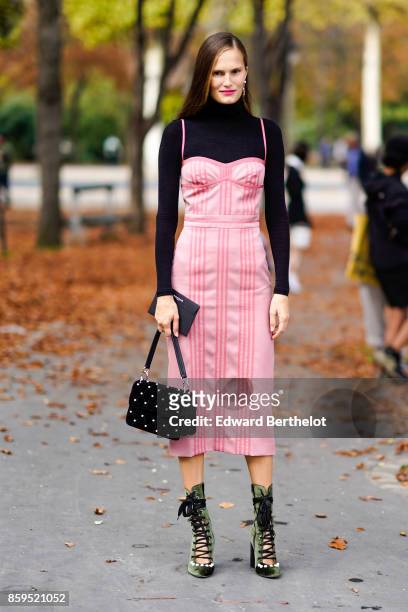 Guest wears a black turtleneck top, a pink striped strapless dress, a black studded bag, green velvet lace-up platform shoes, outside the Rochas...