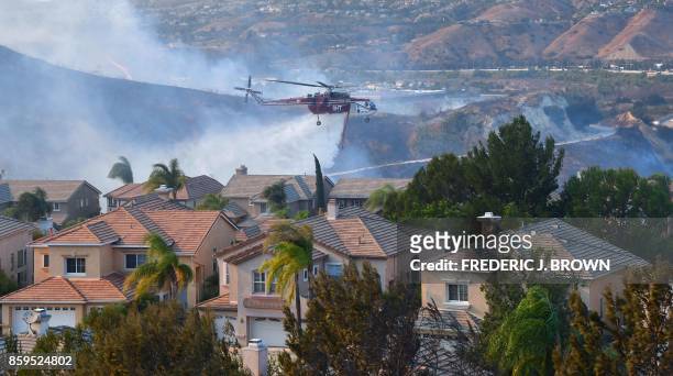 Helicopter drops water near homes at the Anaheim Hills neighborhood in Anaheim, California on October 9 after a fire spread quickly through the area...