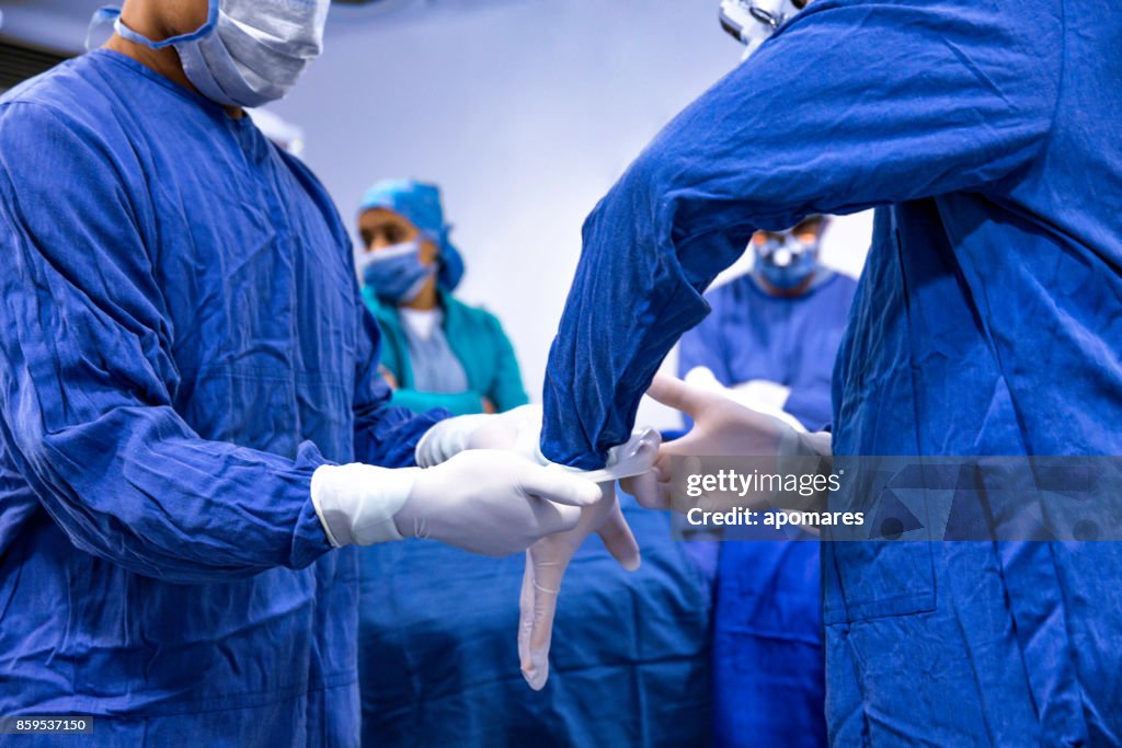 Close-up of Surgeon getting ready for surgical procedure. Assistant helping set surgical gloves.