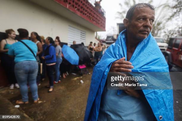 Arian Rodriguez covers himself with a tarp as residents wait in the rain to register with FEMA more than two weeks after Hurricane Maria hit the...